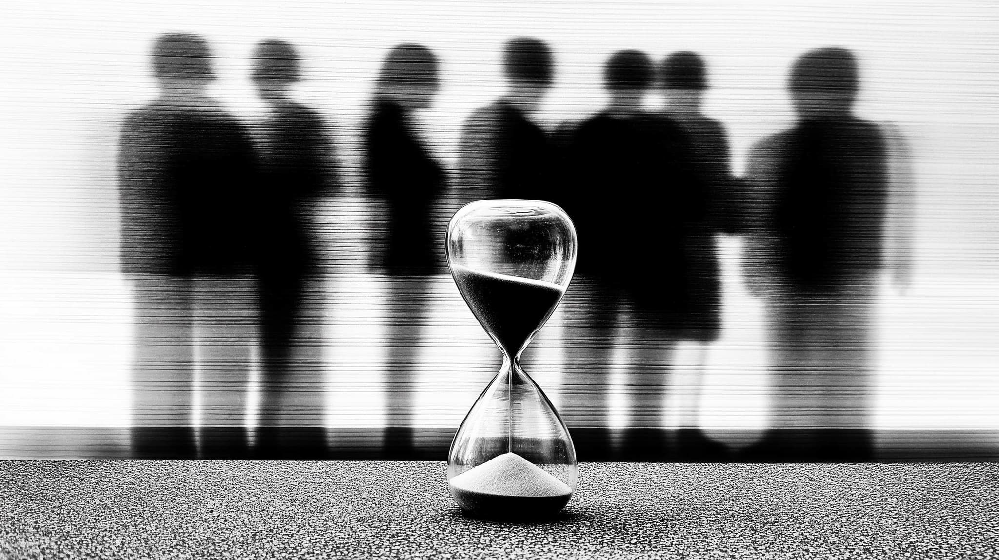 Hourglass with silhouettes of business people in the background, symbolizing how collection agencies maintain stability through economic cycles while internal teams fluctuate